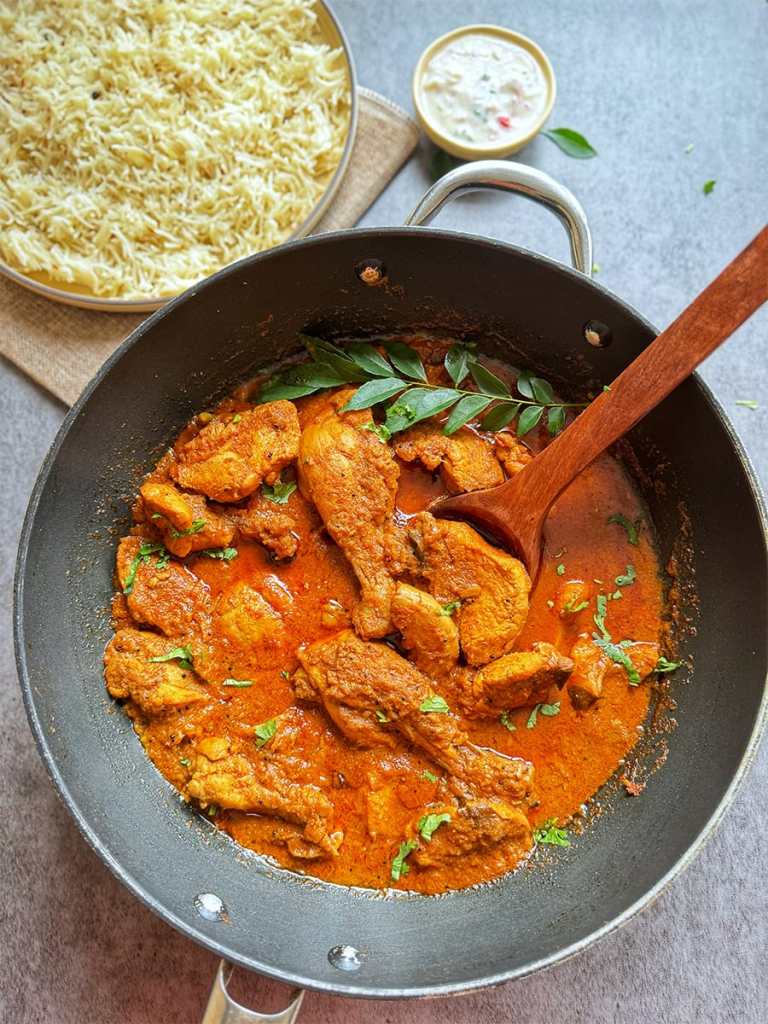 CHICKEN MASALA IN A POT WITH A SERVING OF RICE AND RAITA