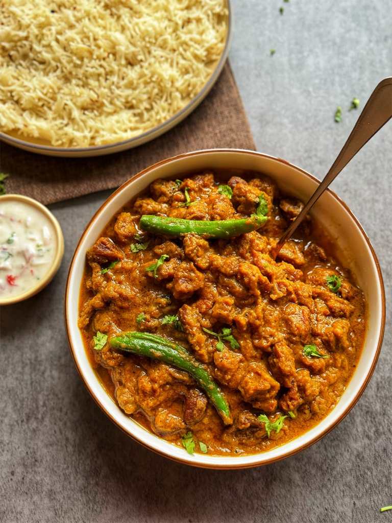 mutton pepper fry in a serving bowl with some ghee rice and raita served at the side