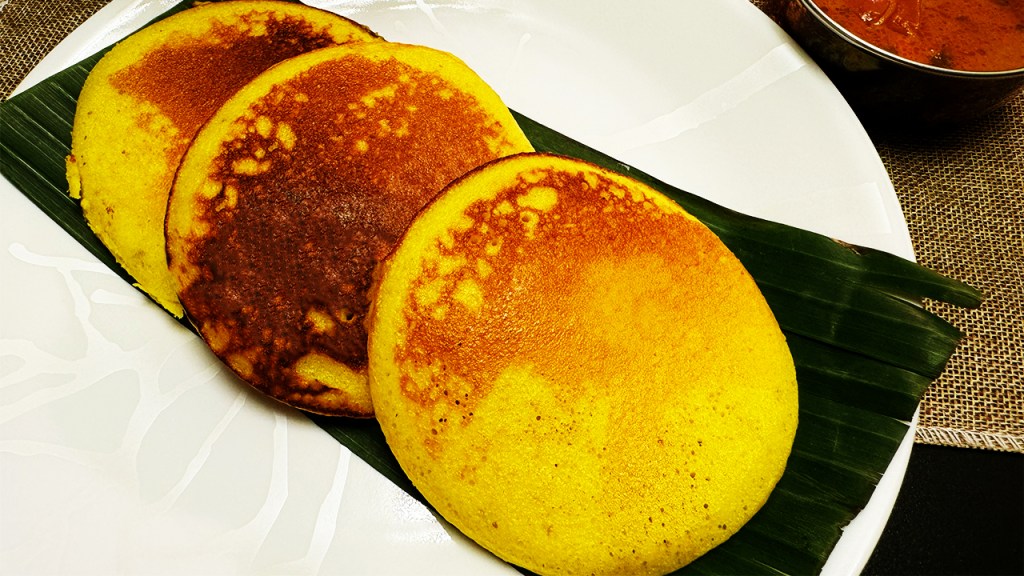 yellow appam being served on a serving plate and dipped into a bowl of fish curry