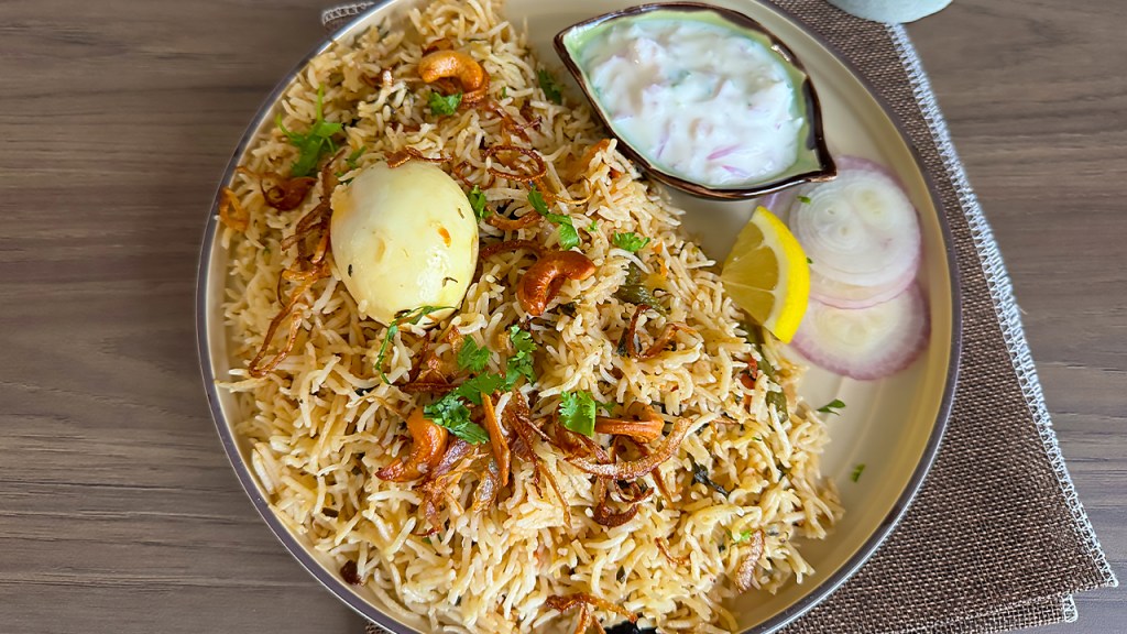 egg biryani on a serving plate with raita, a slice of lemon and sliced onions on the side
