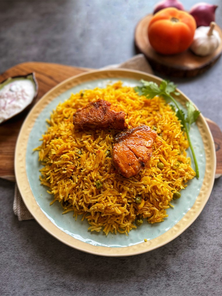 fish biryani on a serving plate with raita on the side