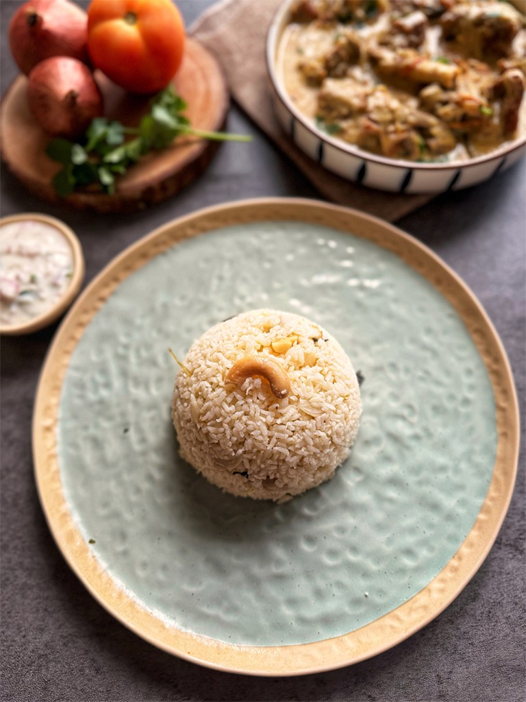 ghee rice in a serving plate with mutton kurma at the side and some onions and tomato to beautify