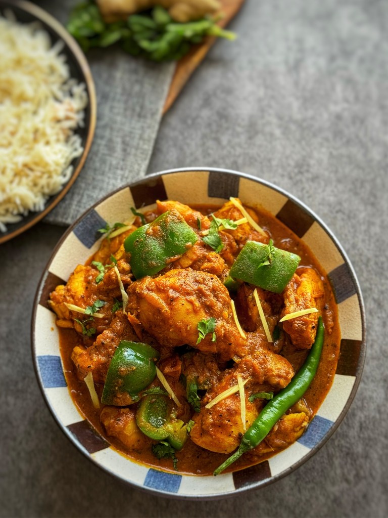 kadai chicken in a serving bowl with a plate of rice at the side