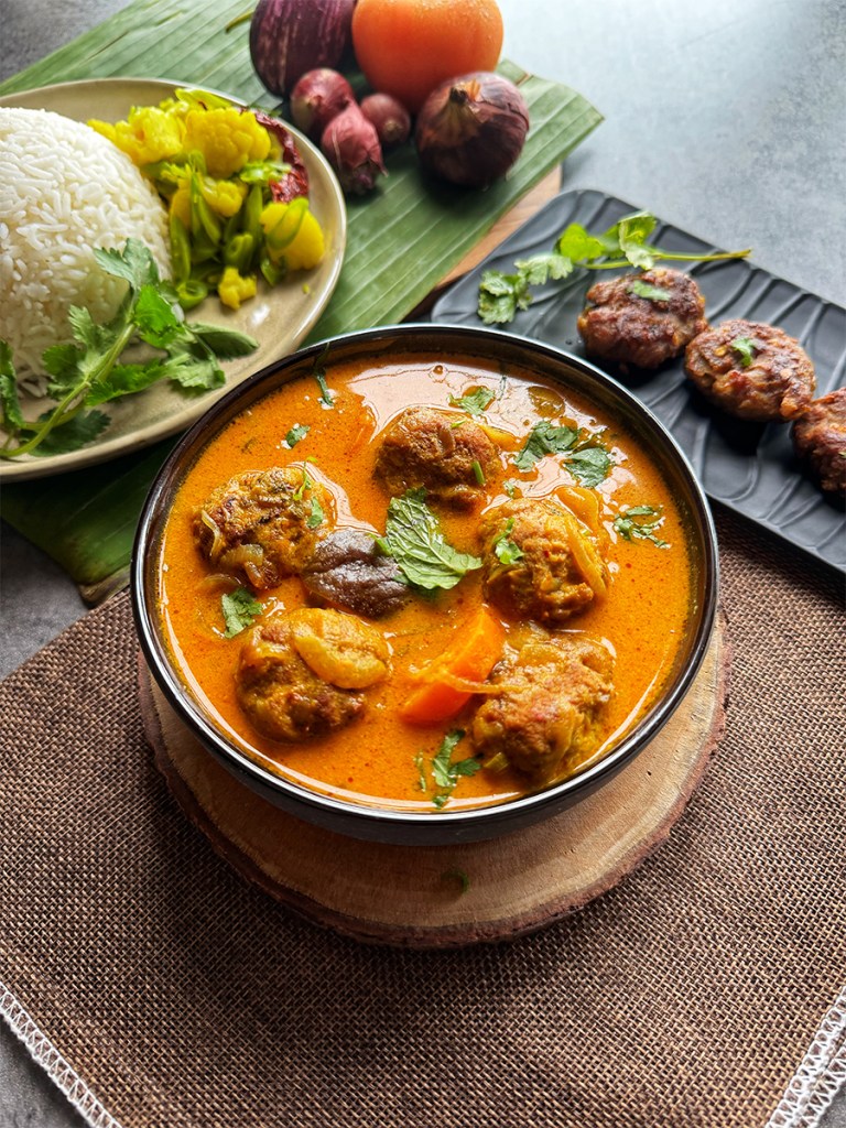 mutton kofta curry on a serving bowl with a bowl of rice vegetable sides and fried mutton kofta at the side