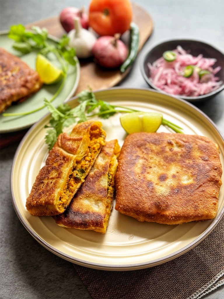 Mughlai Paratha with a slice of lemon wedge and a stalk of coriander leaves with some onion dressings on the side