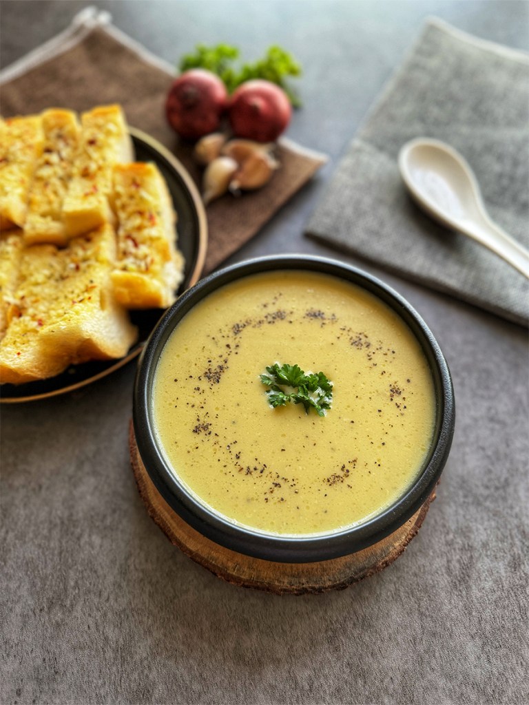 creamy vegetable soup in a serving bowl with garlic bread on a plate
